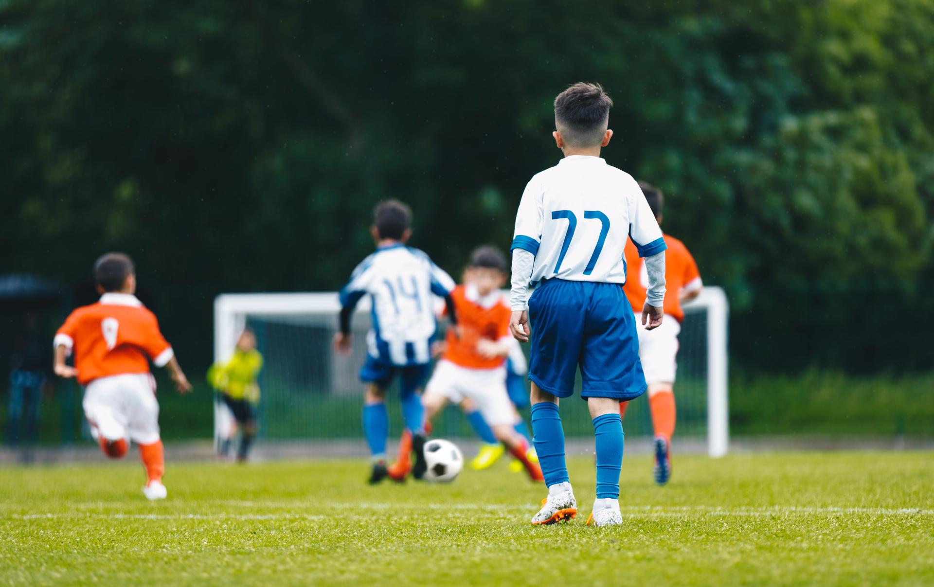 Young school boys playing soccer game. European soccer match between youth teams. Junior competition between players running and kicking a soccer ball. Tournament game between red and blue kids' teams